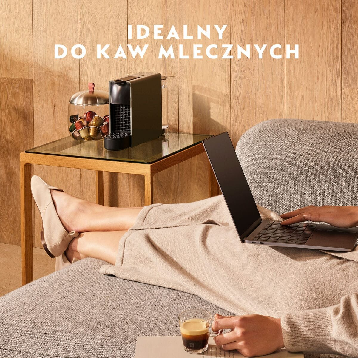 Kobieta korzystająca z laptopa. Na stole filiżanka kawy i ekspres do kawy.