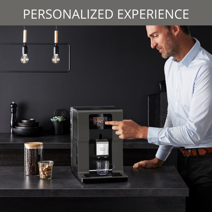 Mężczyzna używa ekspresu do kawy. Ciemny blat, słoiki i czarne tło. Światła nad nim.