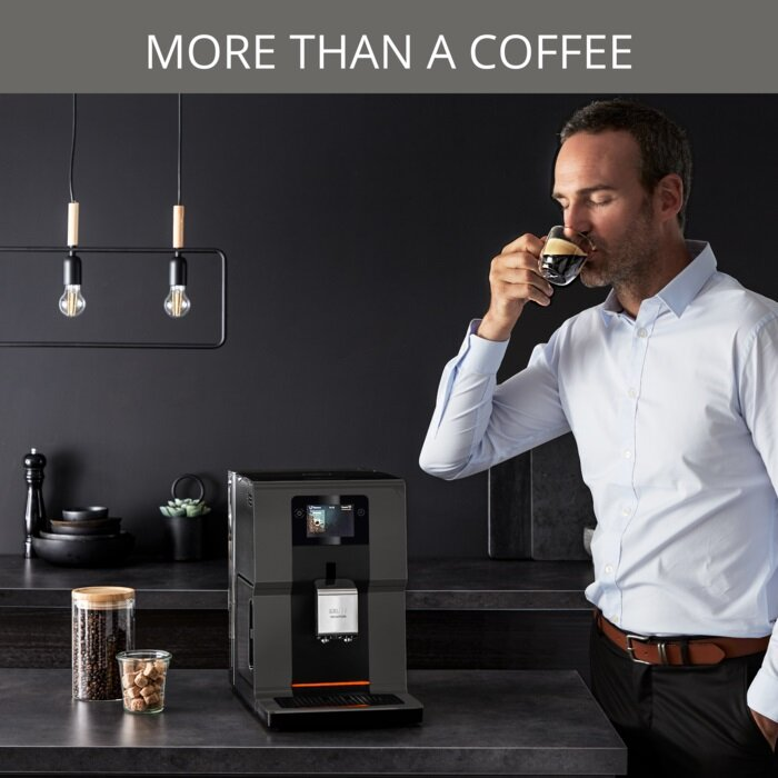 Mężczyzna pije kawę ze szklanki w pobliżu czarnego ekspresu do kawy na czarnym stole.