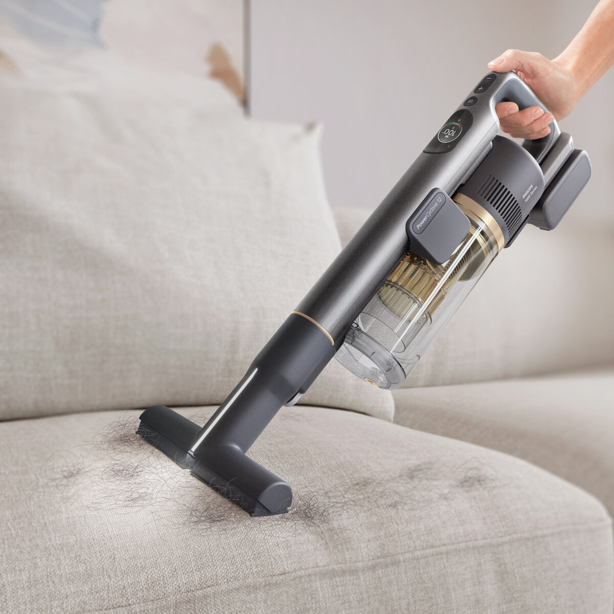 Osoba odkurzająca szarą sofę, usuwająca włosy odkurzaczem ręcznym.