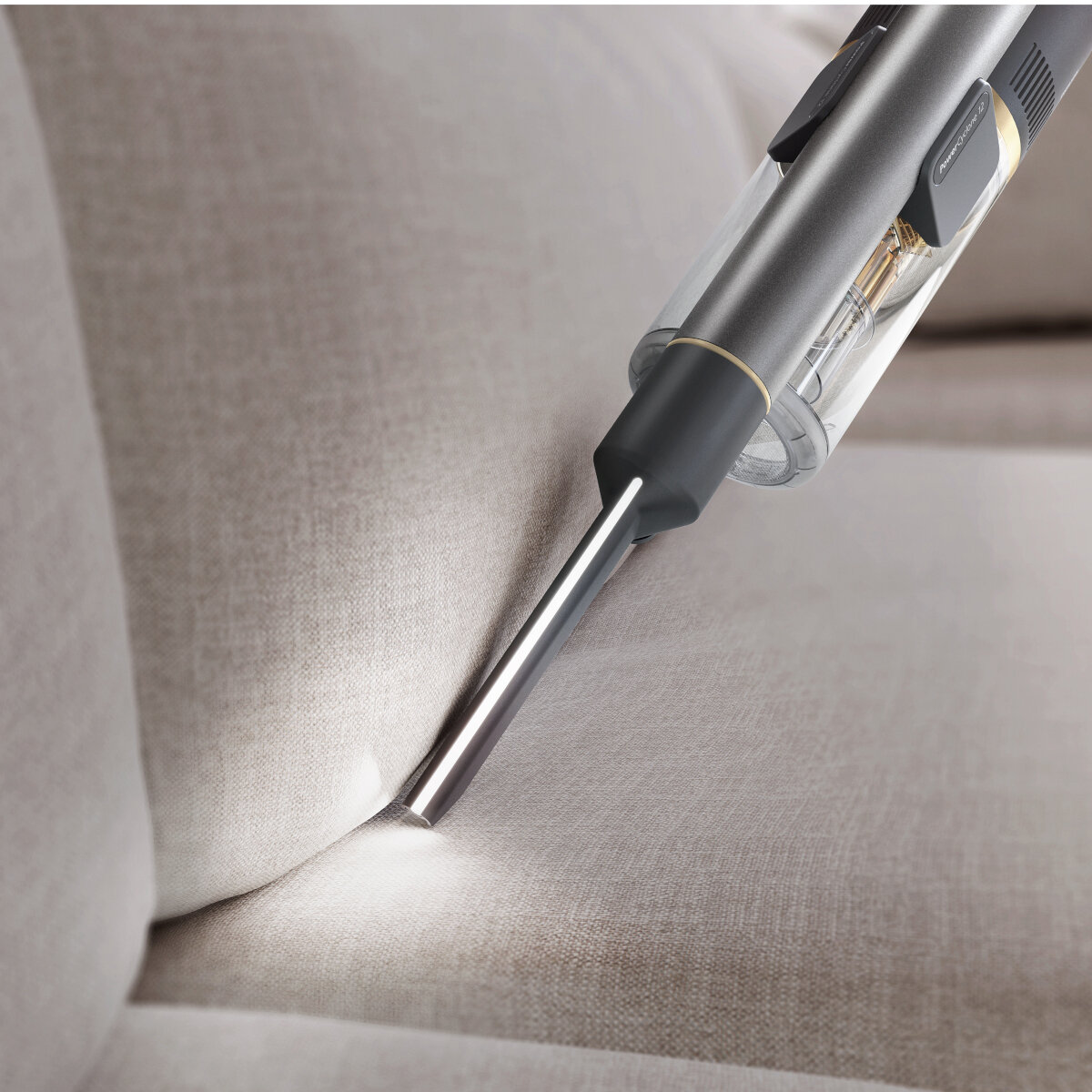 Srebrny odkurzacz ze światłem czyści szarą sofę. Z bliska, dysza dotyka materiału.