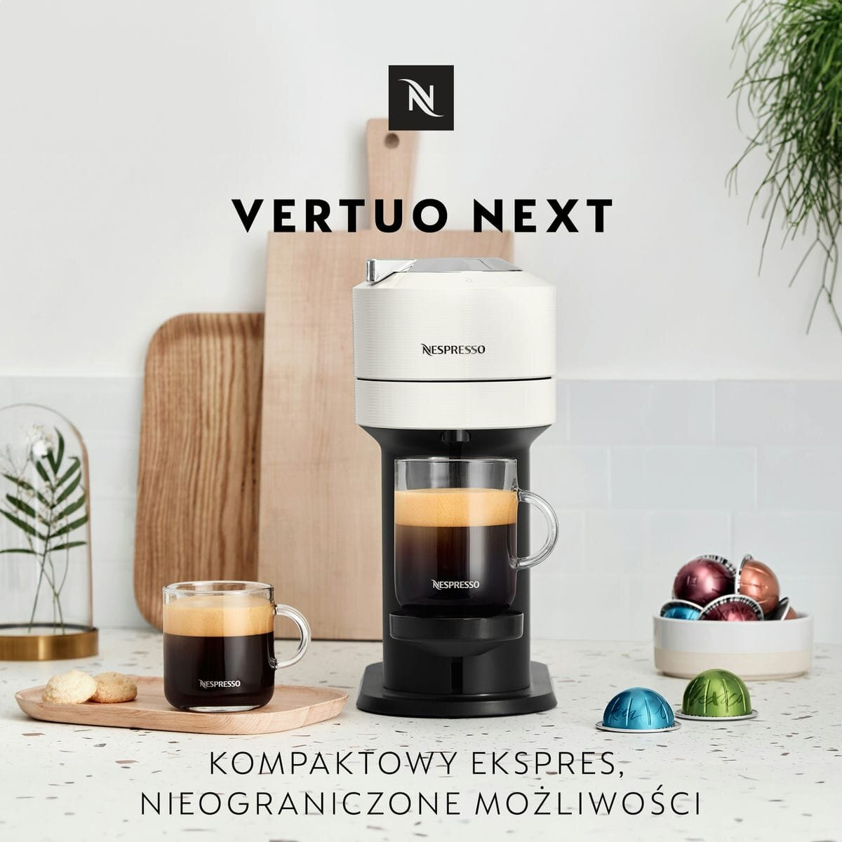 Ekspres do kawy Nespresso Vertuo Next z dwiema filiżankami kawy. Widoczne różne kapsułki.