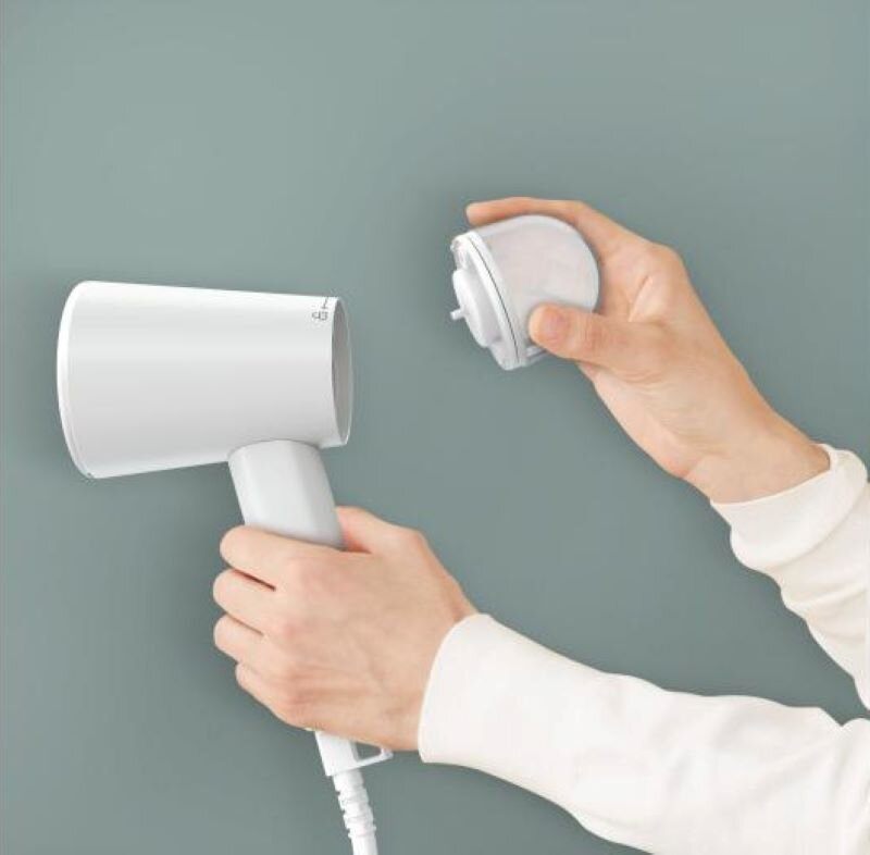 Osoba trzyma białą suszarkę do włosów i jej filtr. Ściana jest jasnozielona.