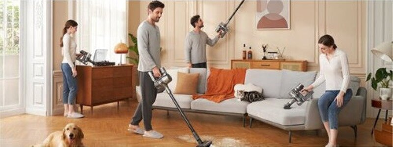 Kilka osób sprząta salon odkurzaczami, w pokoju jest pies.