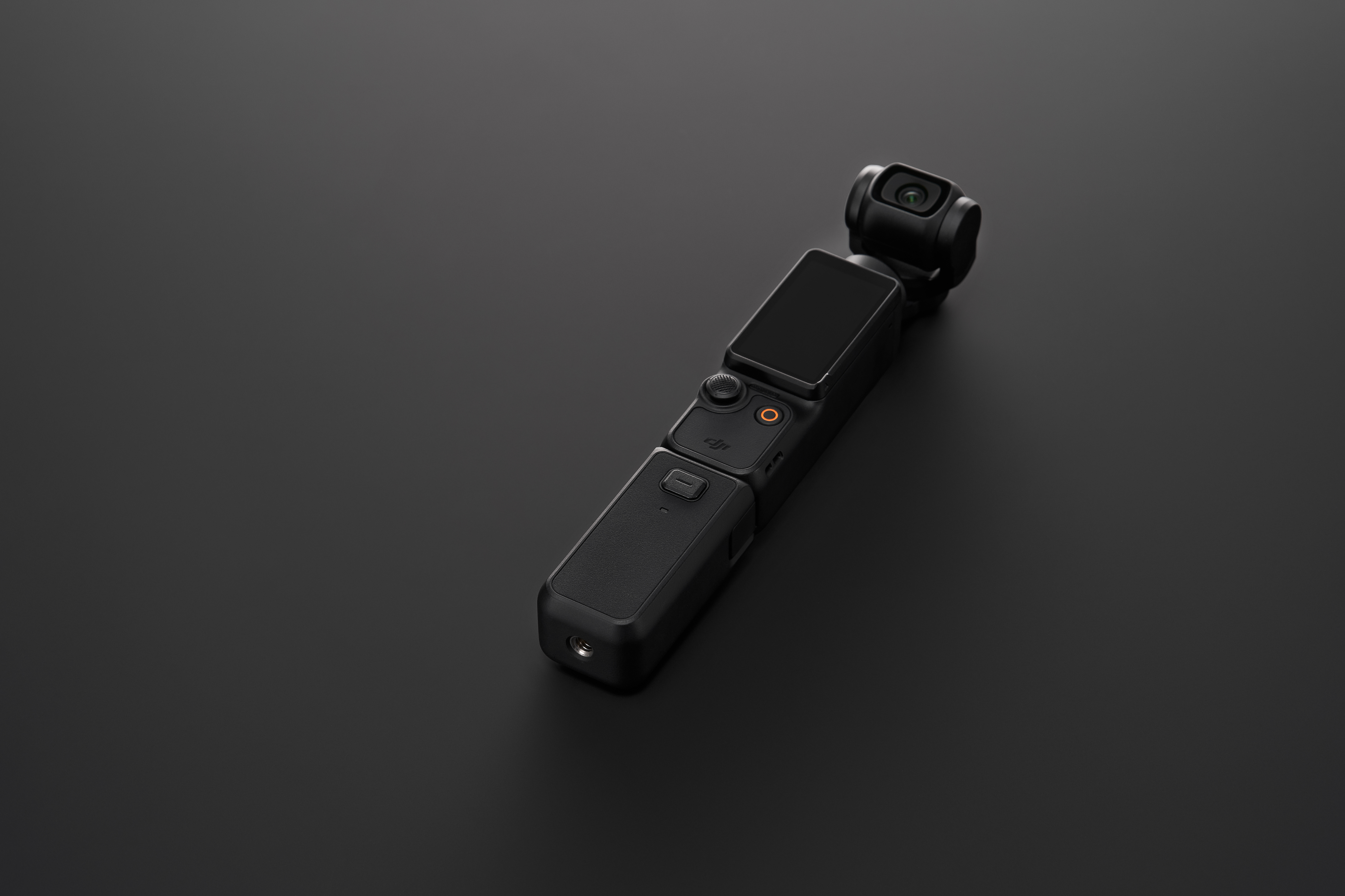 Une caméra DJI Pocket noire sur une surface noire. C'est une petite caméra portable avec un écran.