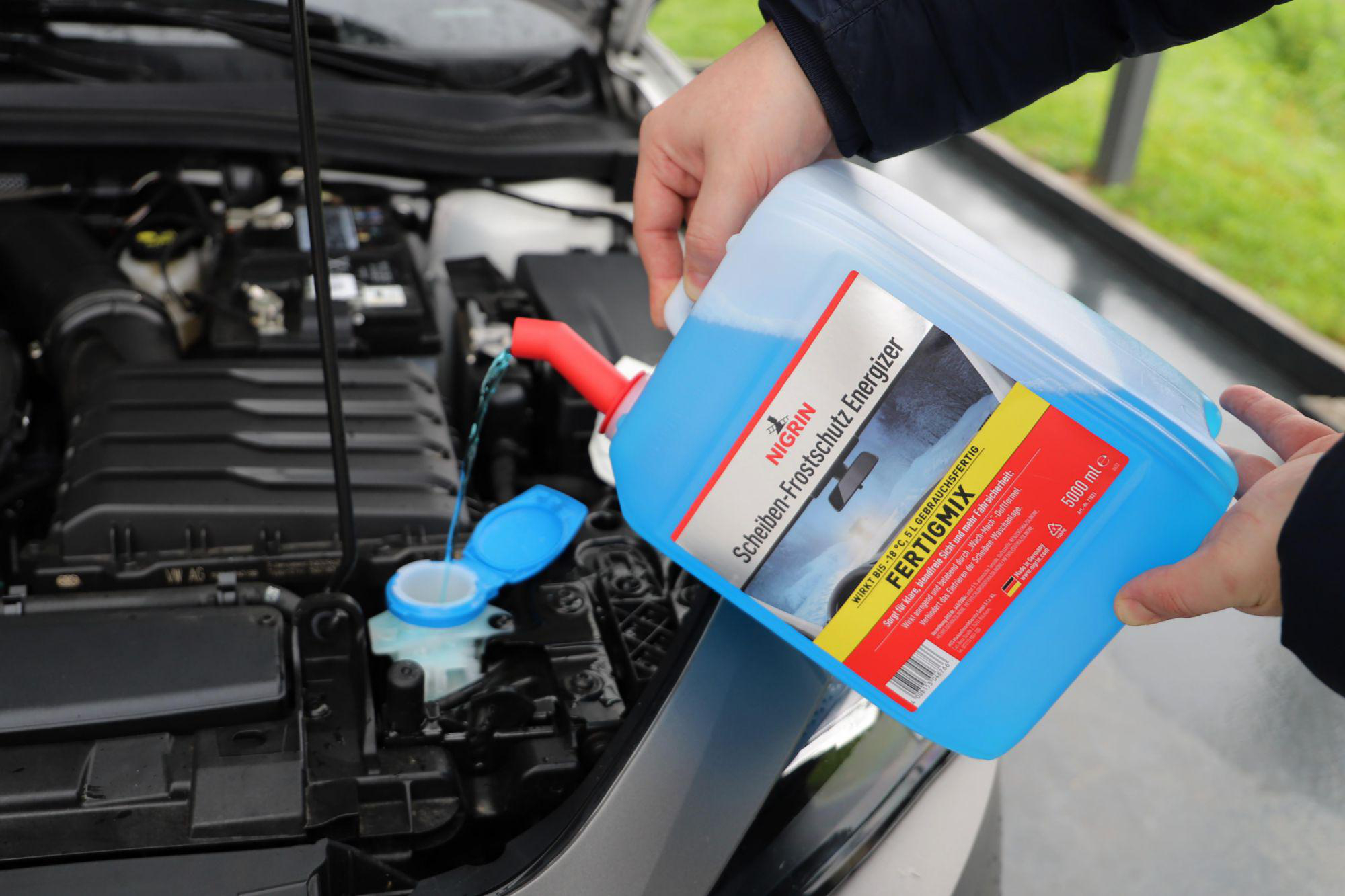 Person gießt blaue Scheibenwaschflüssigkeit in einen Automotor.