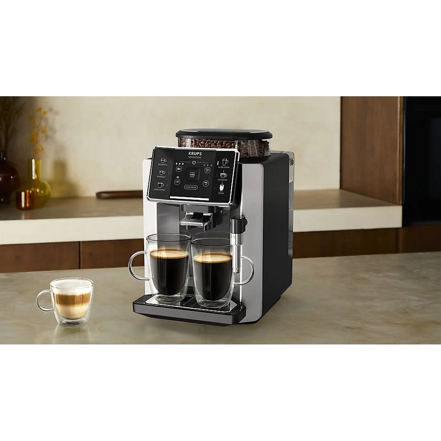 Zwart-zilveren koffiemachine met twee glazen koffiekopjes en een latte.