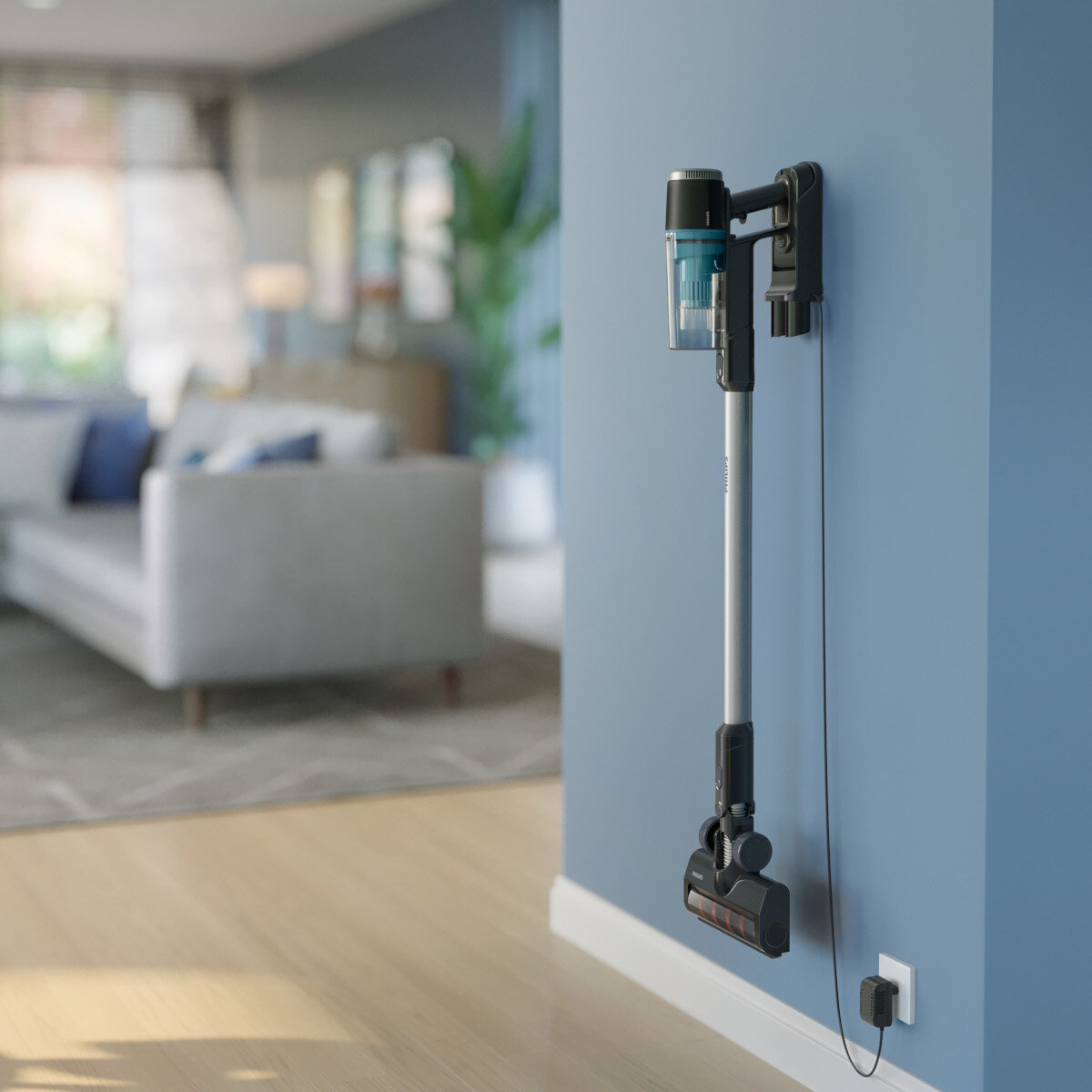 Odkurzacz bezprzewodowy zamontowany na niebieskiej ścianie w pokoju z podłogami z twardego drewna i szarą sofą.