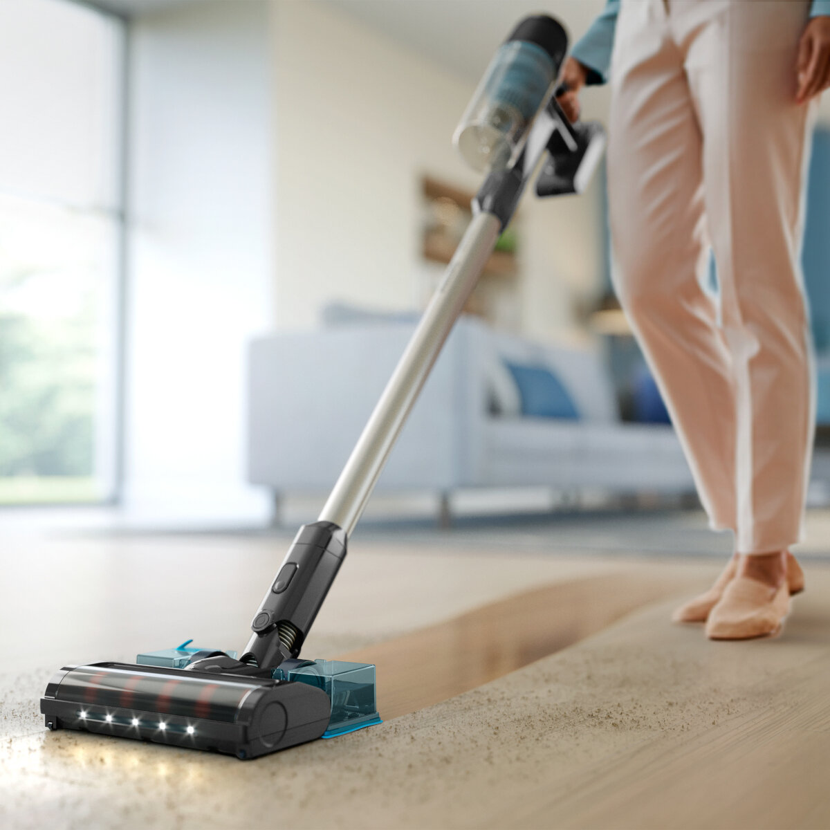 Kobieta odkurzająca drewnianą podłogę nowoczesnym odkurzaczem bezprzewodowym.