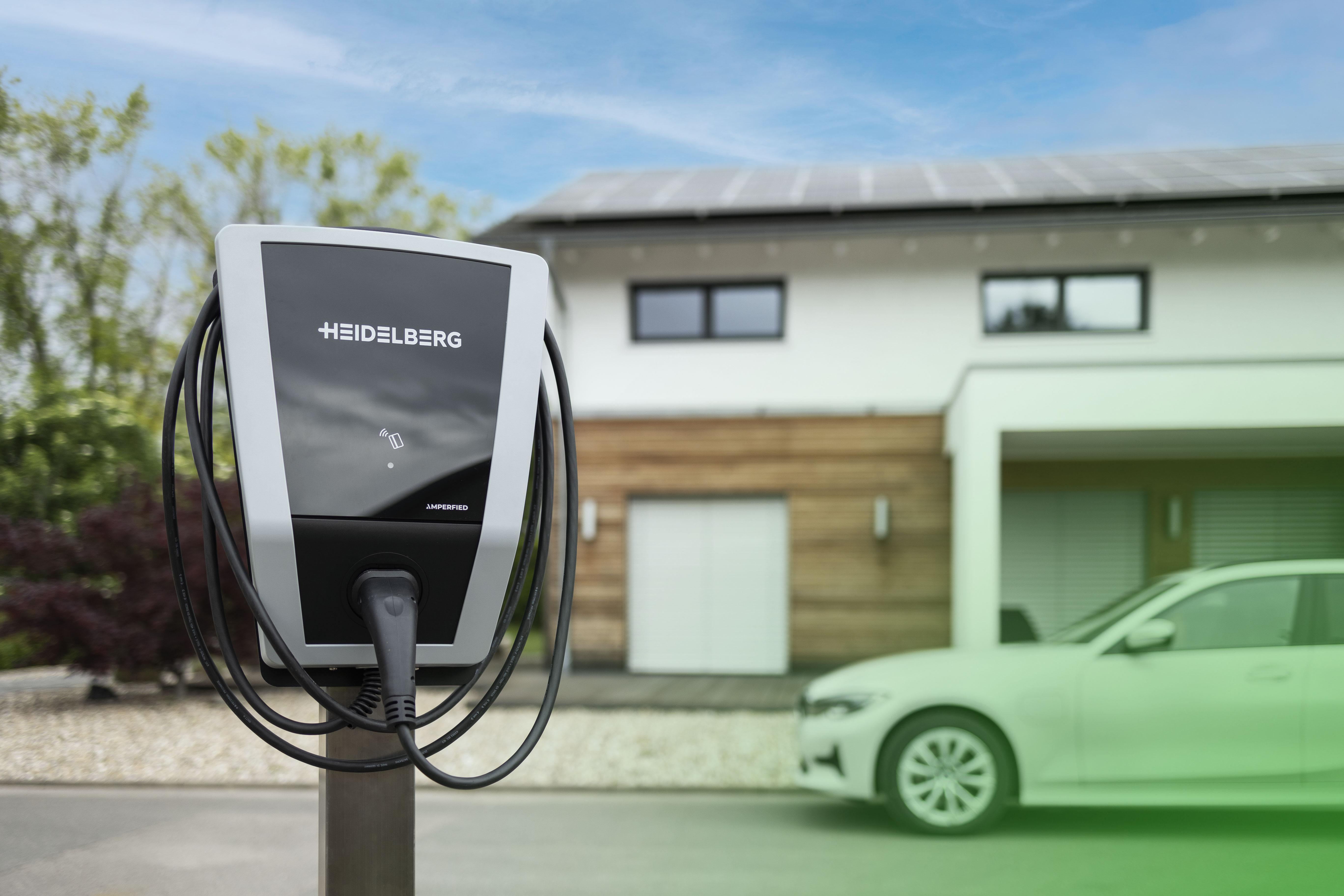 Eine Ladestation mit dem Logo 'Heidelberg', ein Auto und ein Haus mit Sonnenkollektoren auf dem Dach.