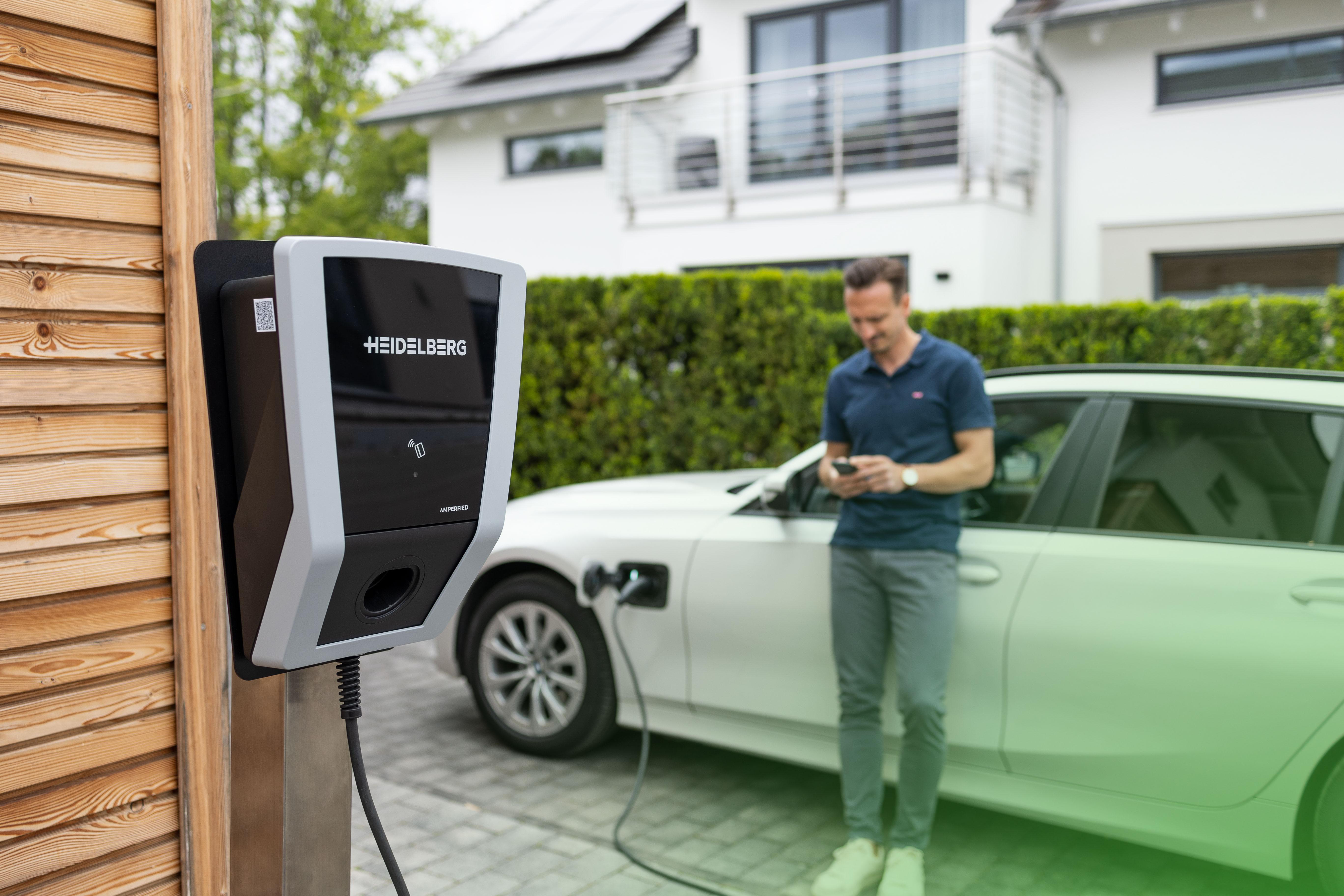 Mann lädt Elektroauto, neben einer schwarz-grauen Ladestation an einer Holzwand.