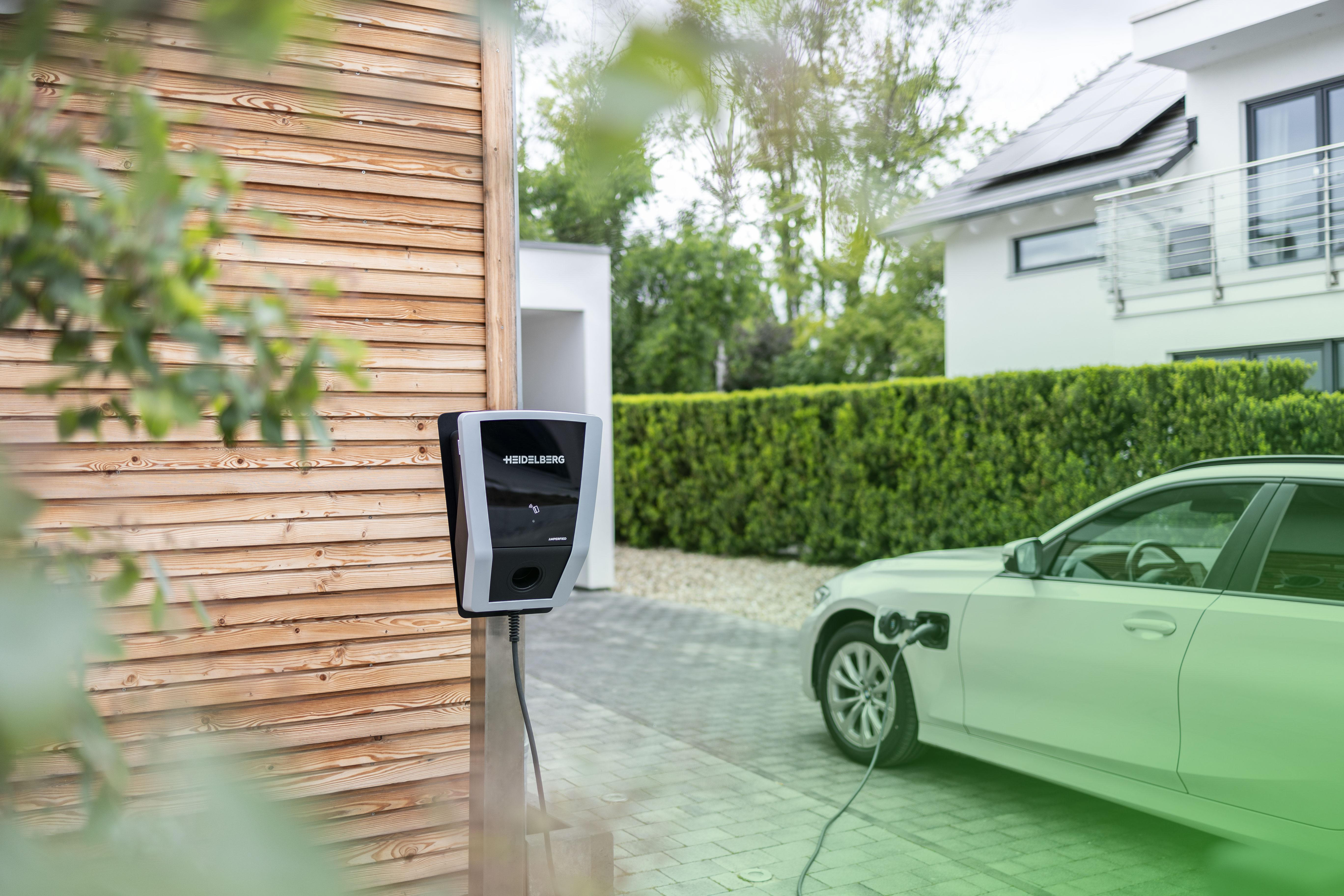 Elektroauto, das an einer Ladestation zu Hause geladen wird, mit Haus mit Sonnenkollektoren.