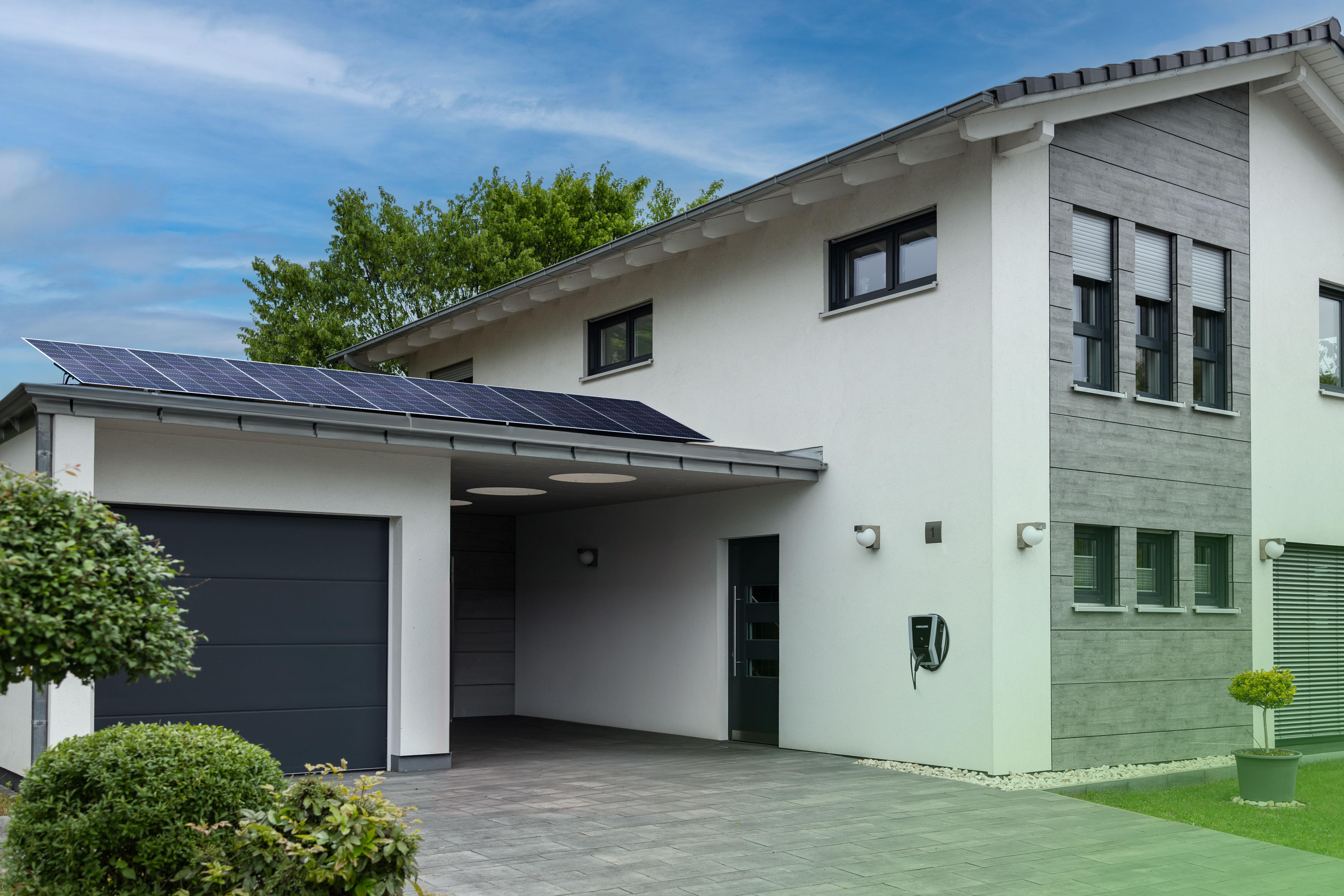 Modernes Haus mit Solarmodulen auf dem Dach, Garage und Rasen. Blauer Himmel im Hintergrund.