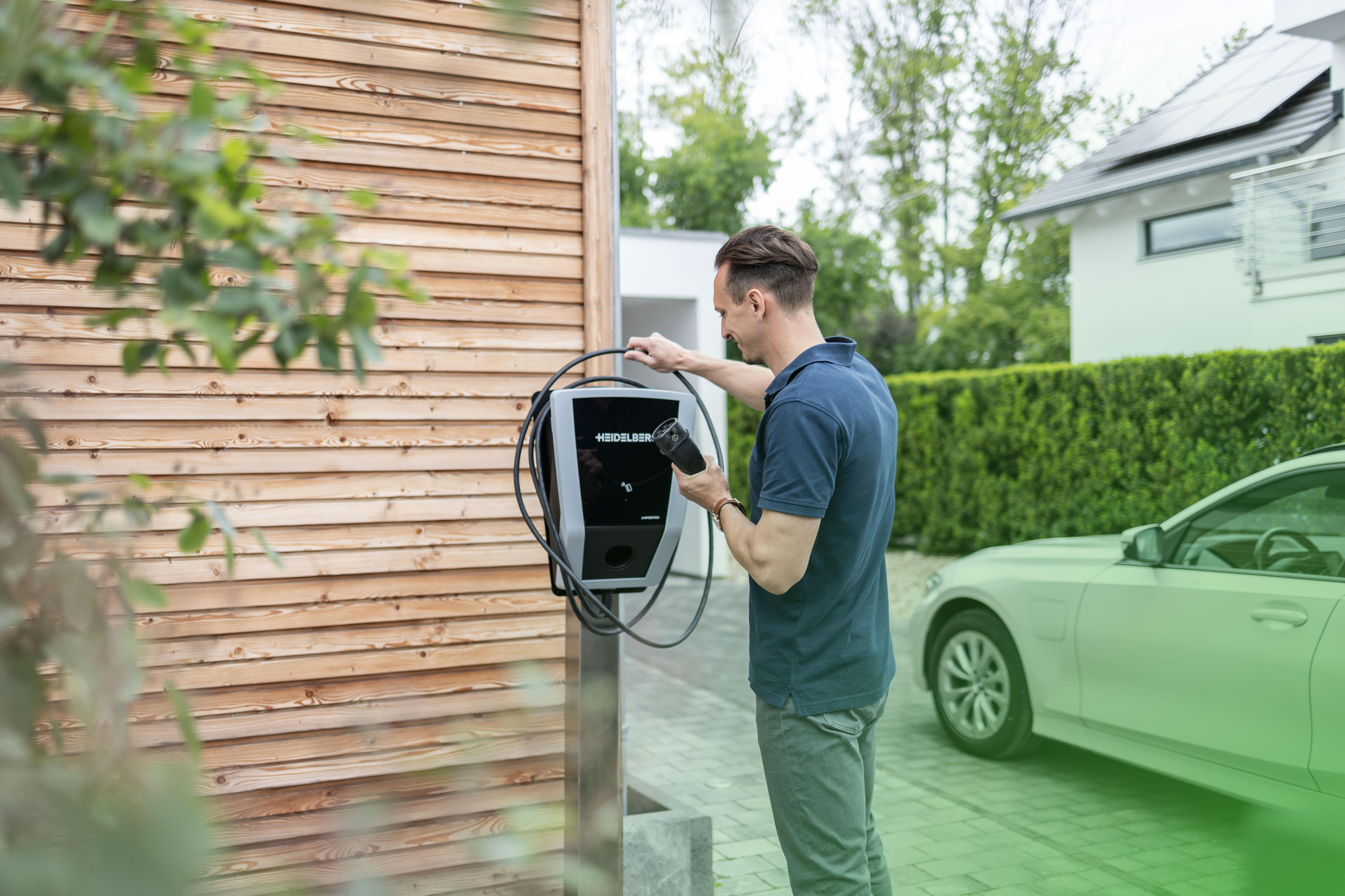Ein Elektroauto parkt vor einem Haus mit Sonnenkollektoren. Eine Ladestation befindet sich an der Wand.