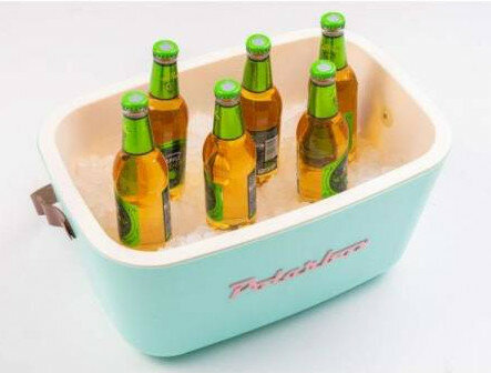 Sześć zielonych butelek piwa w niebieskiej lodówce wypełnionej lodem. Lodówka ma różowe logo.