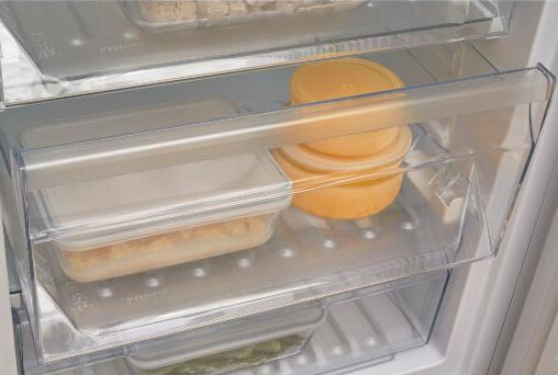 Wewnątrz lodówki. W środku znajdują się przezroczyste pojemniki z jedzeniem.