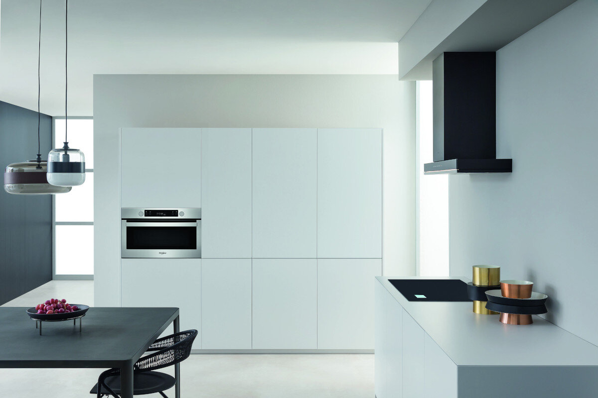 Nowoczesna kuchnia. Są białe szafki, kuchenka mikrofalowa i czarna płyta grzewcza.