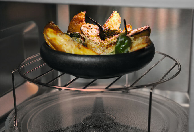 Jedzenie w czarnej misce na ruszcie kuchenki mikrofalowej. Jedzenie jest pieczone i zawiera ziemniaki.