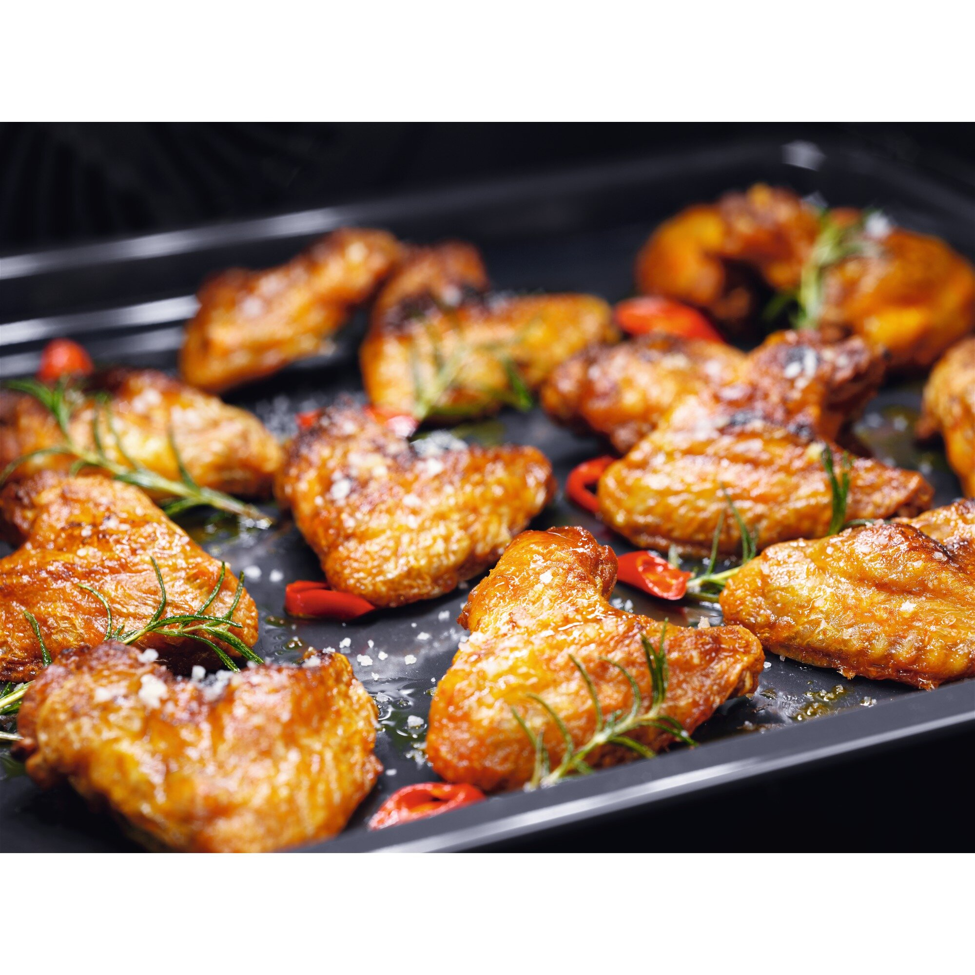 Pieczone skrzydełka z rozmarynem i papryczkami chili na ciemnej tacy.