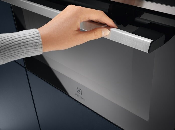 Ręka otwiera drzwi piekarnika. Piekarnik jest czarny i ma srebrny uchwyt. Logo Electrolux.