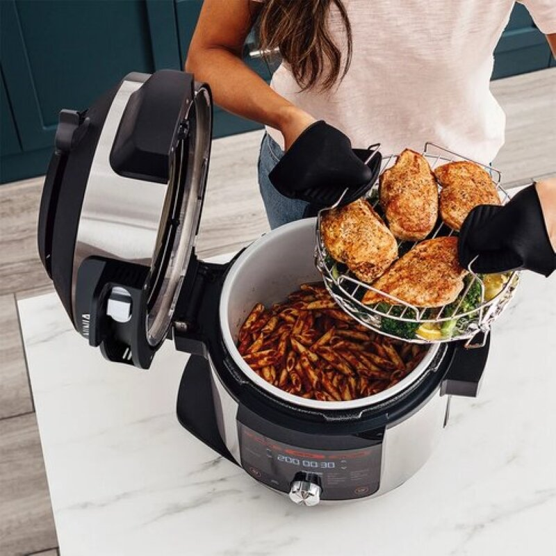 Kobieta trzyma kosz z ugotowanym kurczakiem w multicookerze Ninja. Makaron w urządzeniu.