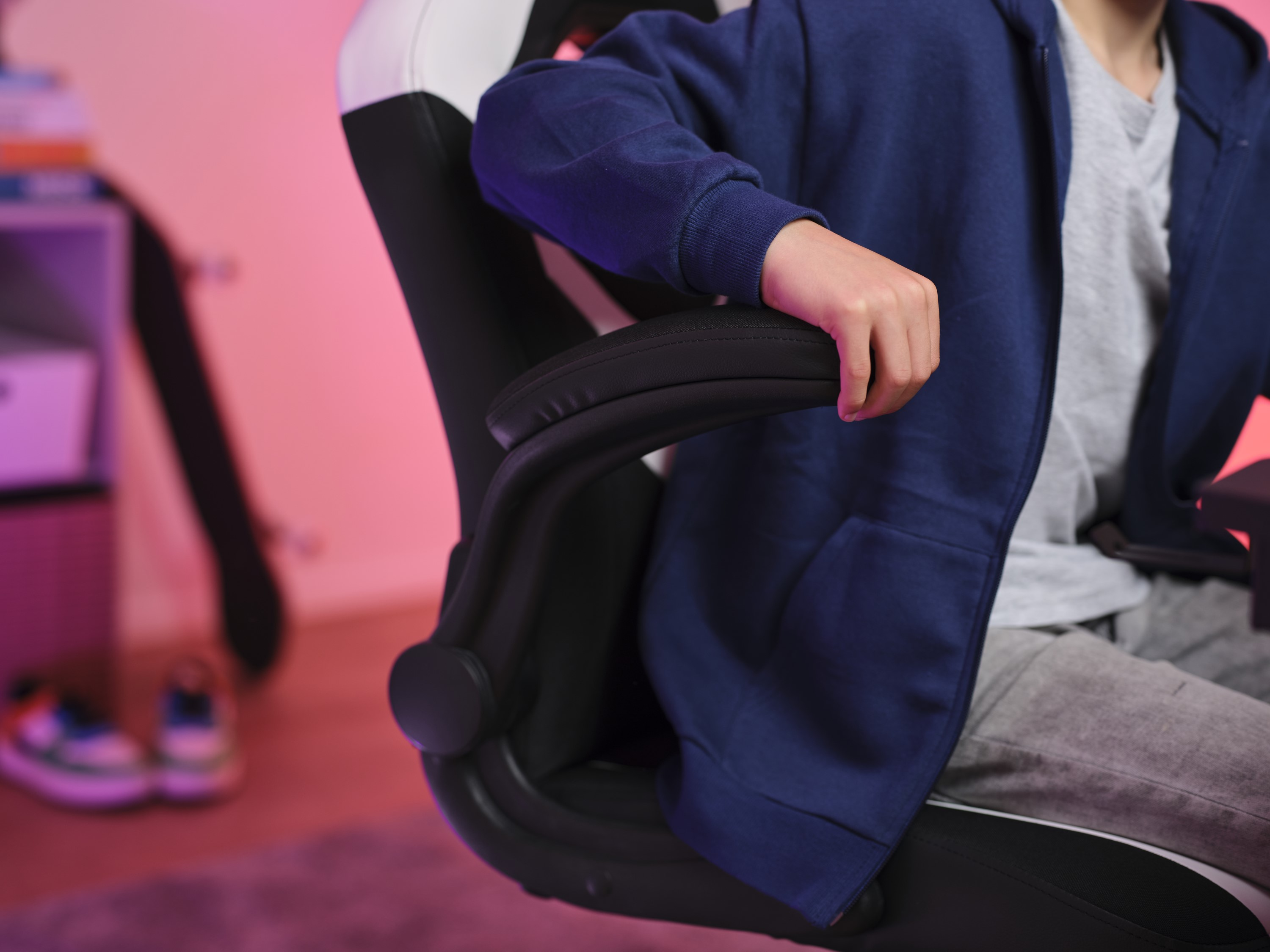 Gros plan sur le bras d'une personne sur une chaise de jeu, avec une veste bleue et un pantalon gris.
