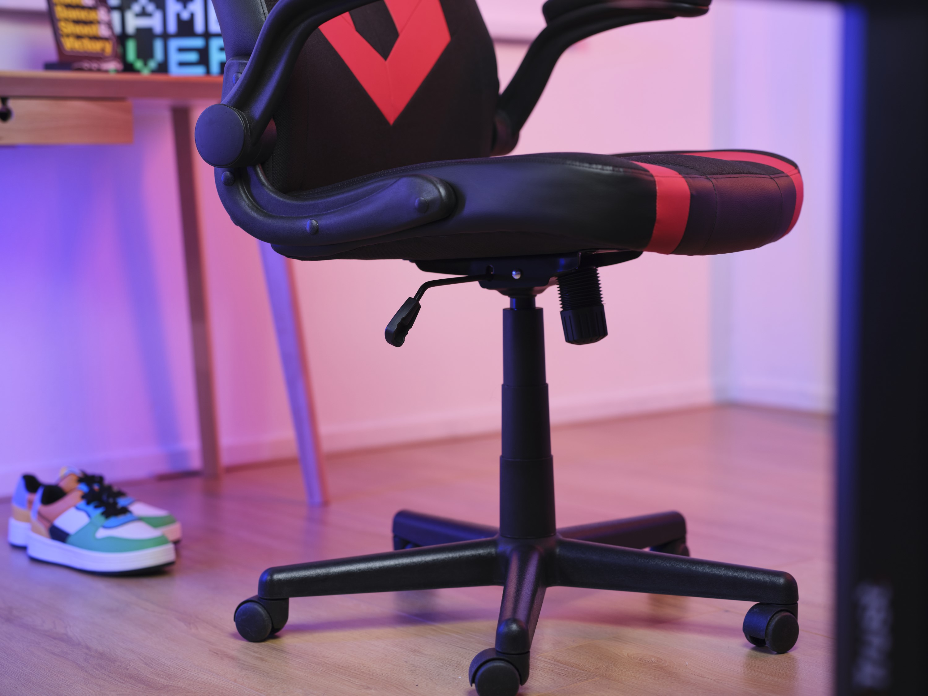Chaise de jeu avec des accents rouges, sur un plancher en bois. Bureau, chaussures et mur en arrière-plan.