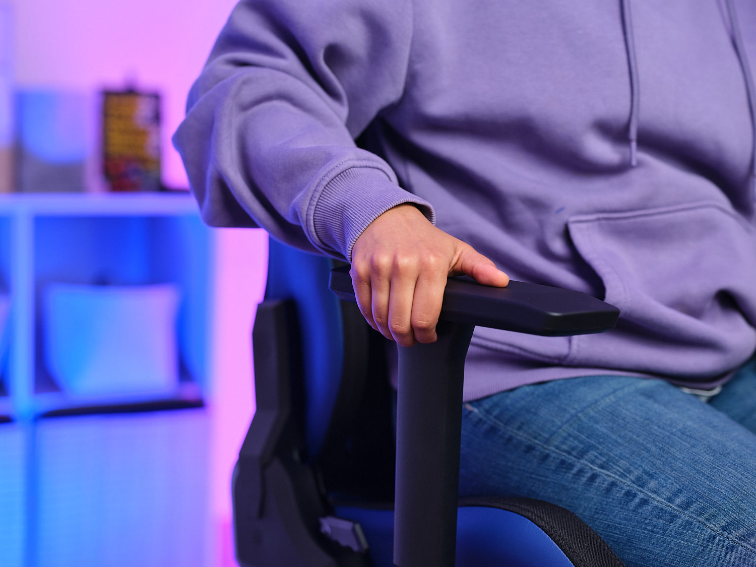 La main d'une personne repose sur l'accoudoir d'une chaise de jeu bleue et noire, visible de la taille vers le haut.