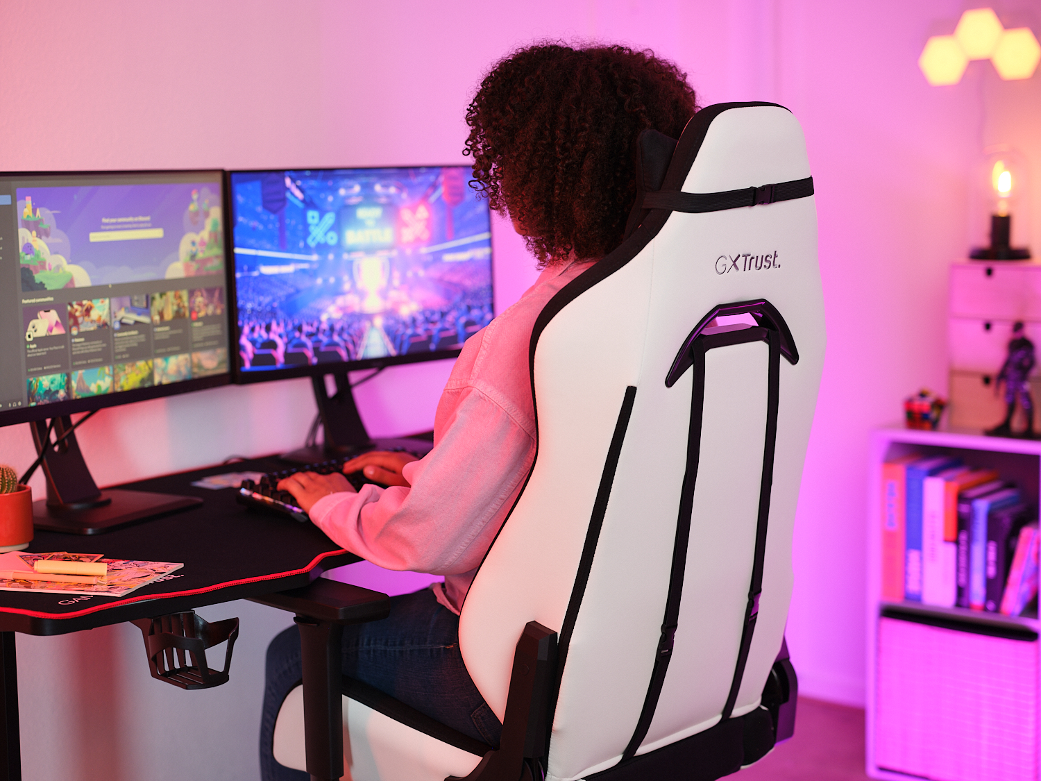 Une personne assise dans un fauteuil de jeu blanc et noir, face à deux moniteurs, tapant sur un clavier.