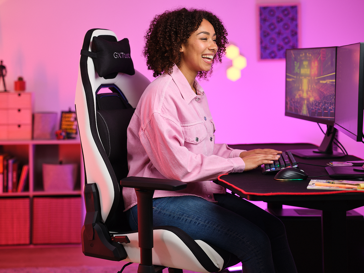 Une femme joue dans un fauteuil de jeu blanc et noir. Un moniteur, un clavier et une souris sur le bureau.