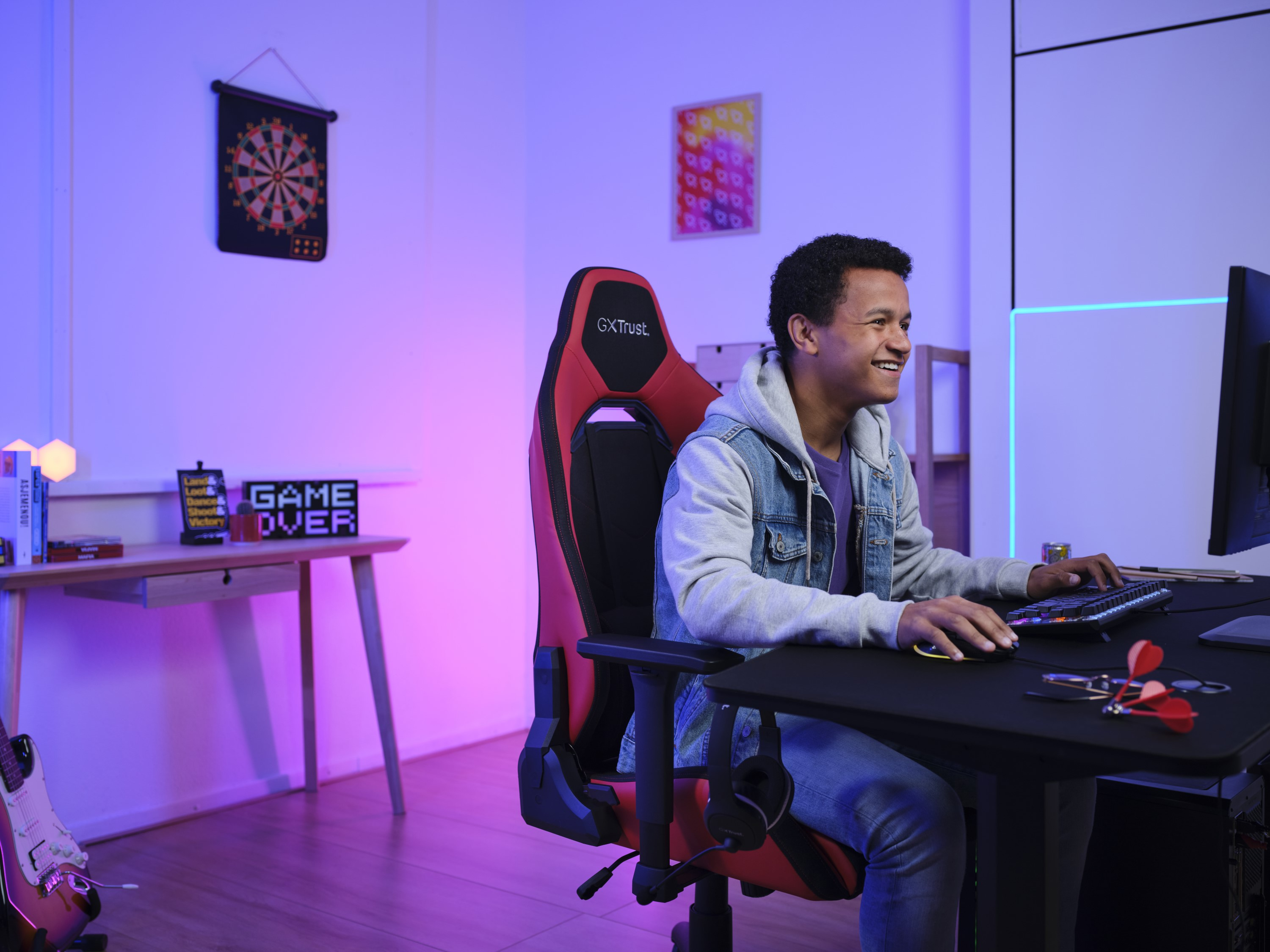 Een jonge man is aan het gamen op een computer, zittend in een rode gamestoel.