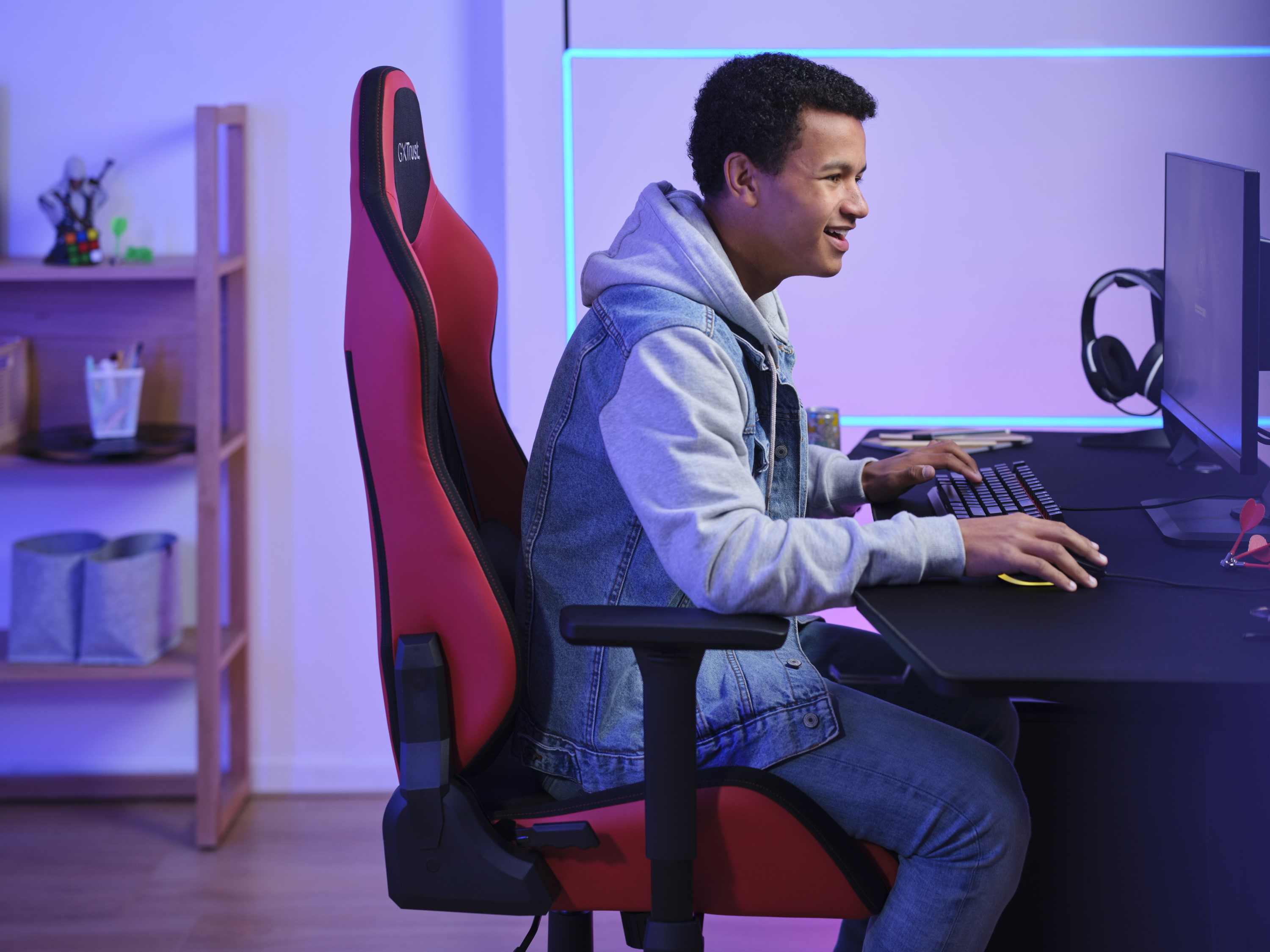Een jonge man speelt een spel op een computer met een rode gamestoel.