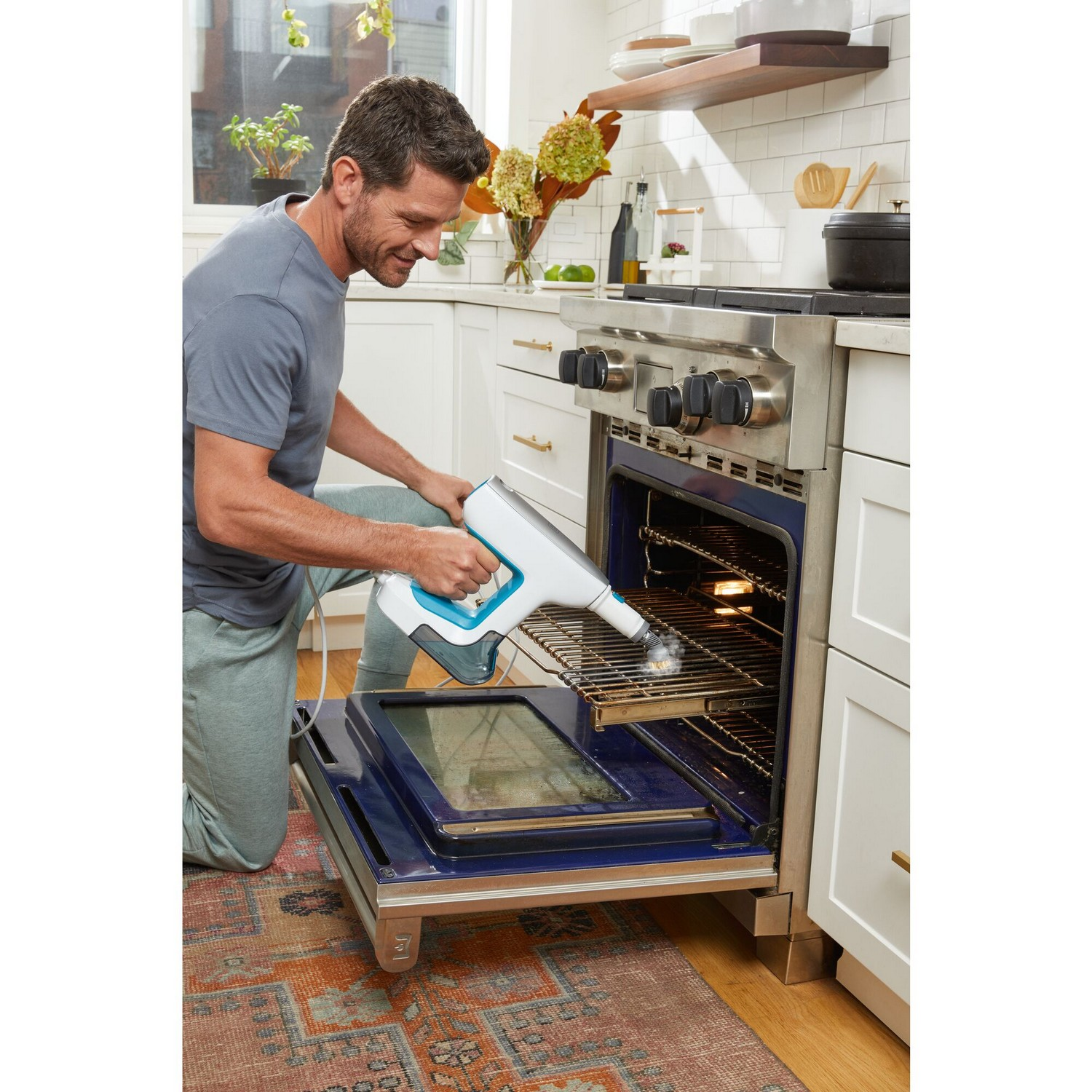 Man die de oven schoonmaakt met een stoomreiniger. Ovendeur open, keuken op de achtergrond.
