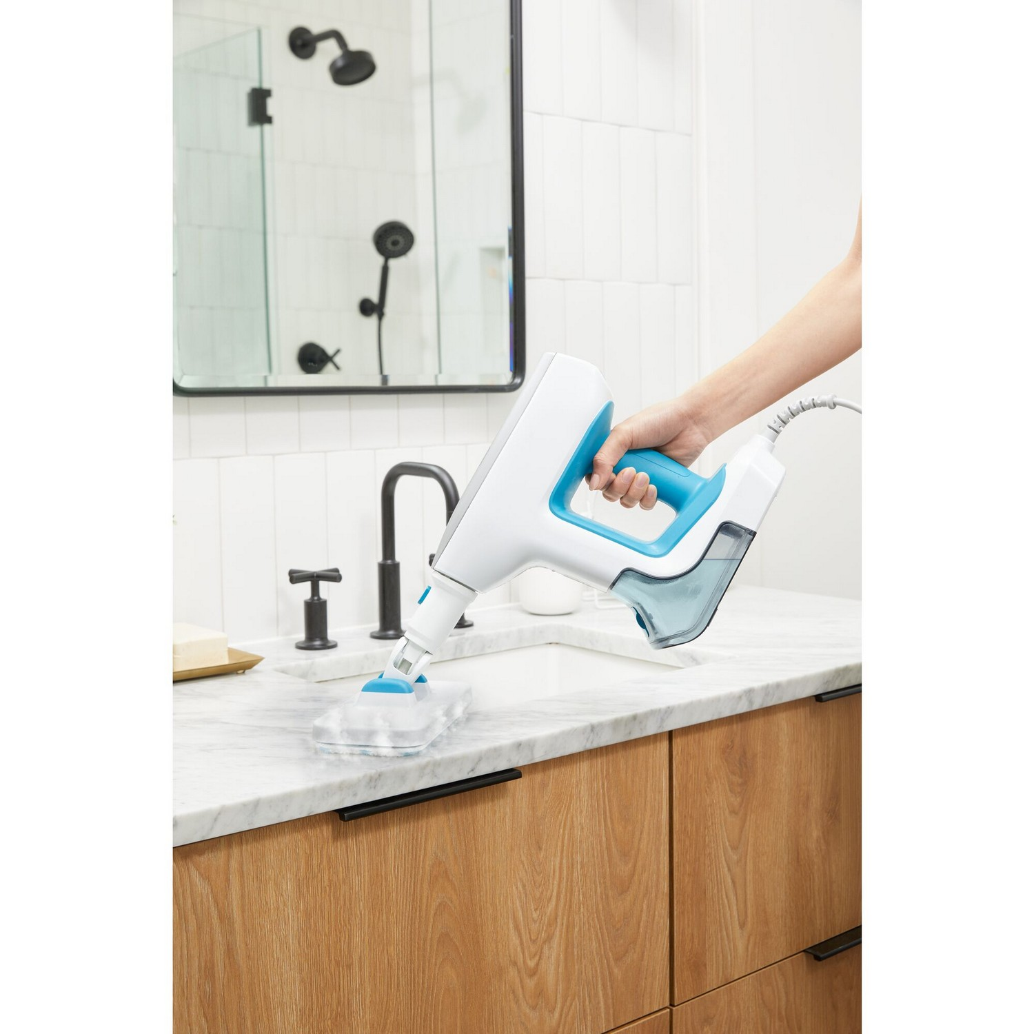 Een persoon gebruikt een witte en blauwe stoomreiniger in een badkamer.
