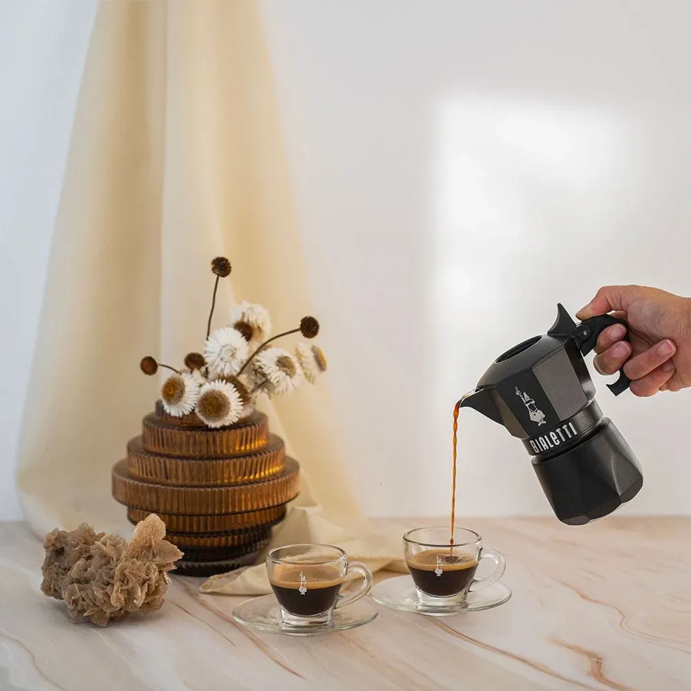 Egy személy kávét önt egy fekete Bialetti mokkakannából két átlátszó üvegpohárba.