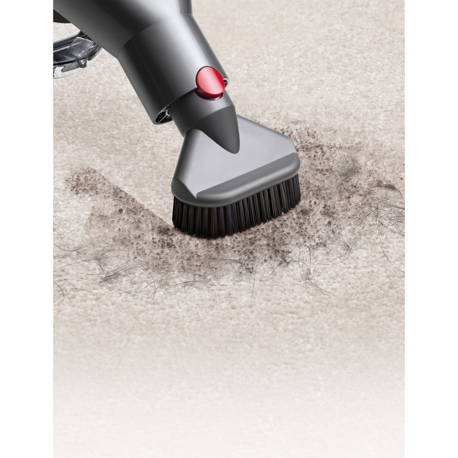 Tête d'aspirateur nettoyant un tapis avec des débris et des cheveux visibles. La brosse est noire.