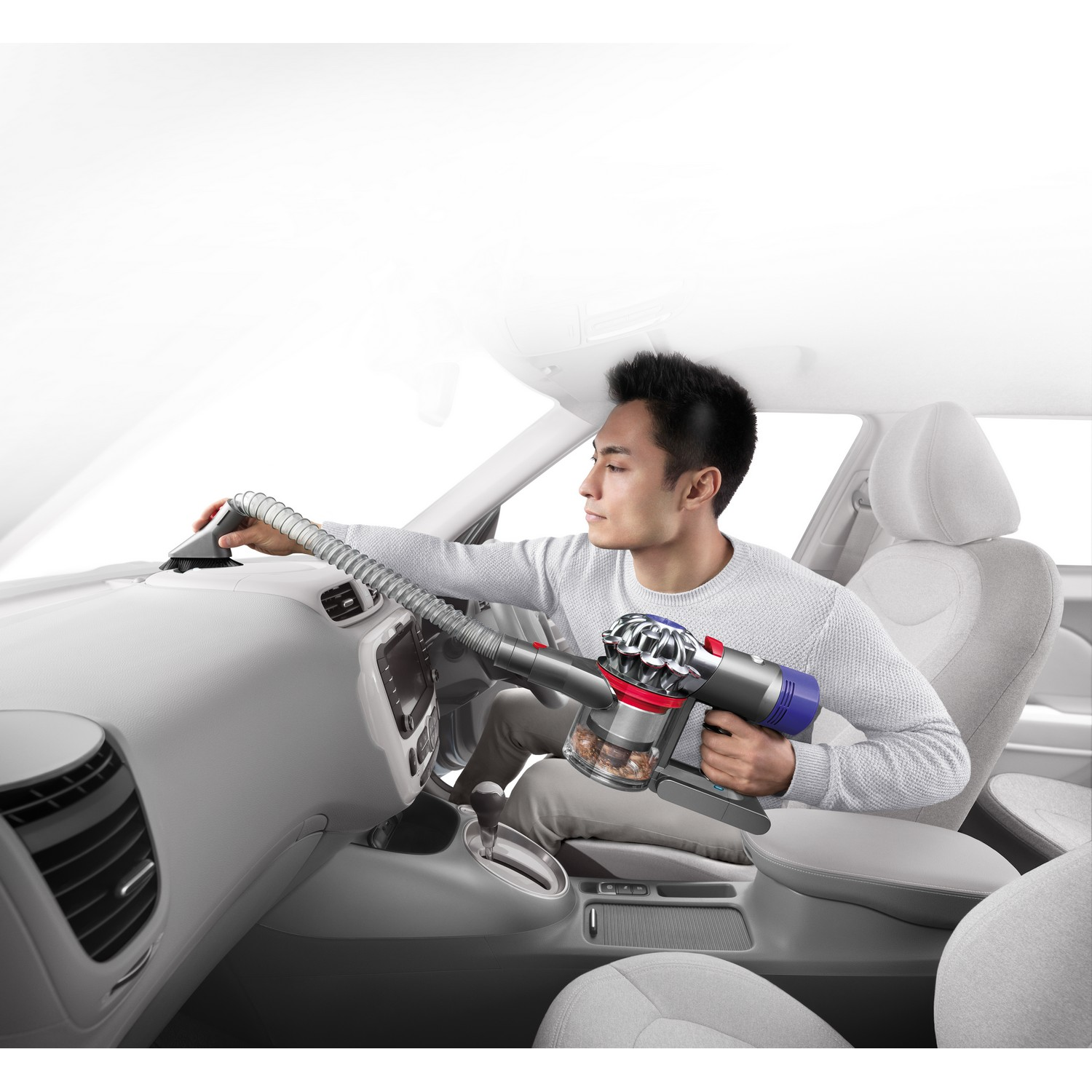 Homme nettoyant intérieur de voiture avec aspirateur Dyson, tableau de bord gris.