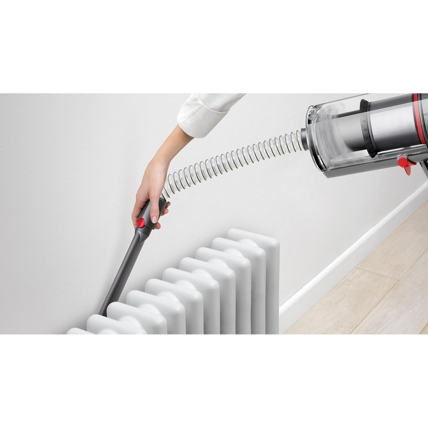Main utilisant une buse d'aspirateur pour nettoyer derrière un radiateur blanc.