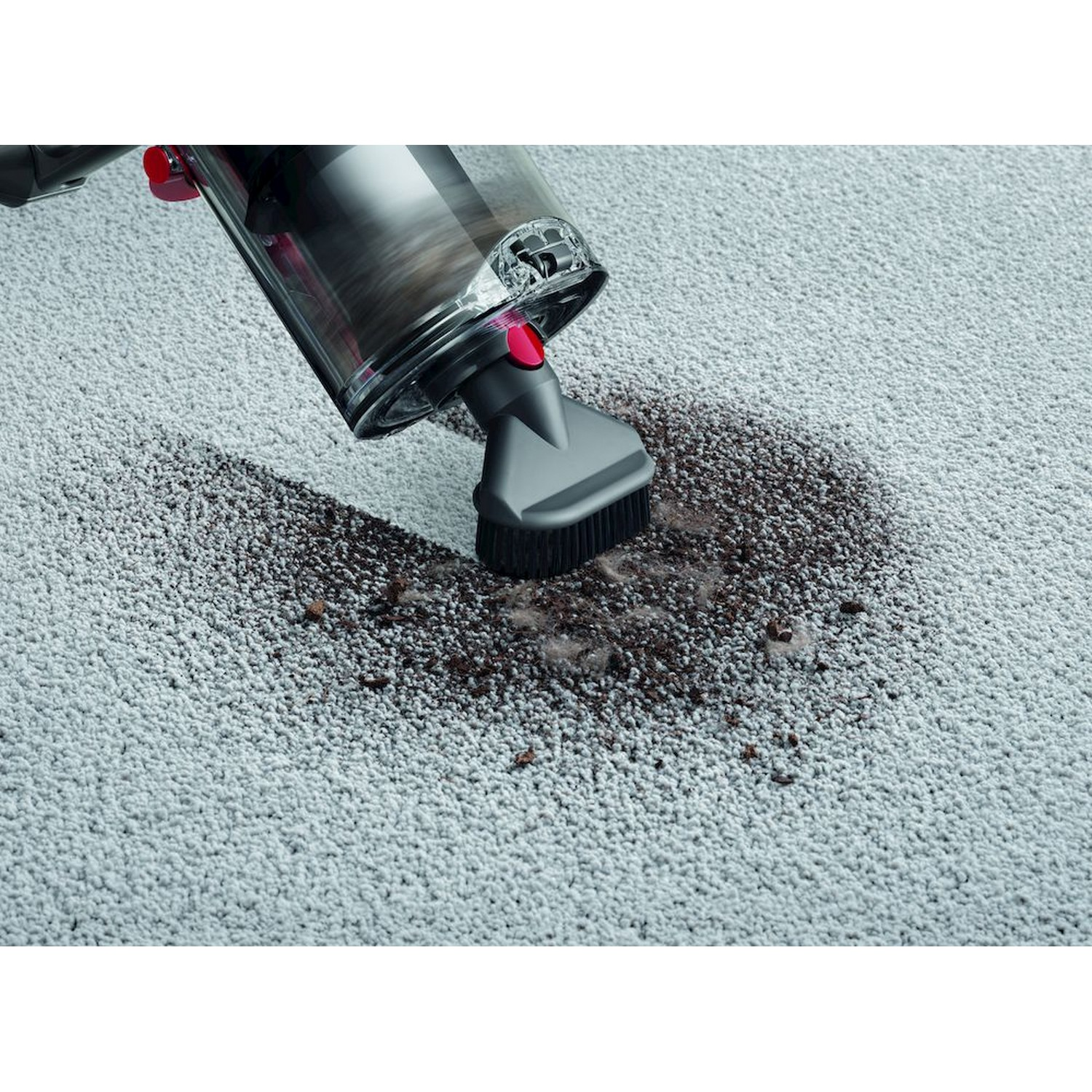 Un aspirateur avec une brosse nettoie une tache sale sur un tapis gris clair.