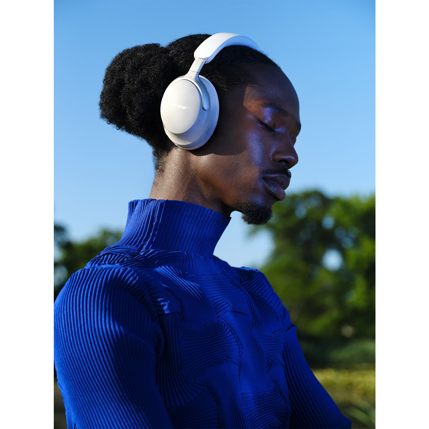 Un uomo di colore con cuffie Bose bianche, dolcevita blu, che guarda lontano dalla fotocamera.