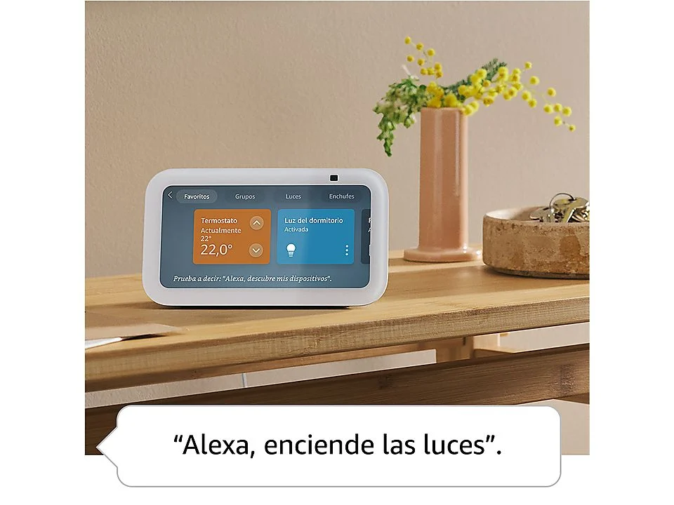 Un Amazon Echo Show 5 en una mesa de madera, mostrando una interfaz de hogar inteligente, cerca de un jarrón y llaves.