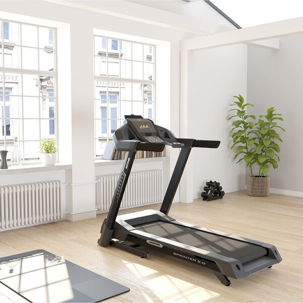 Bieżnia w jasnym pokoju z oknami, matą i sprzętem do ćwiczeń.