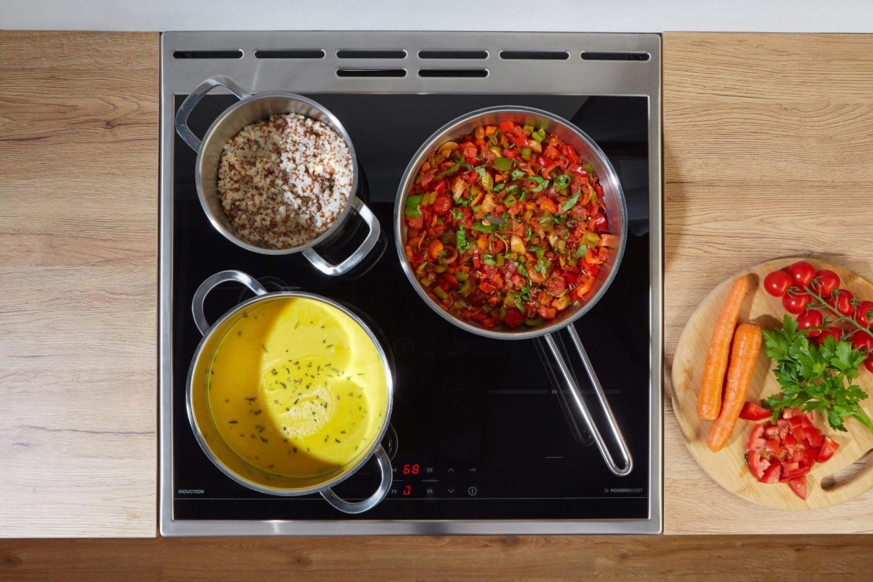 Płyta indukcyjna z trzema patelniami: ziarna, warzywa, zupa.