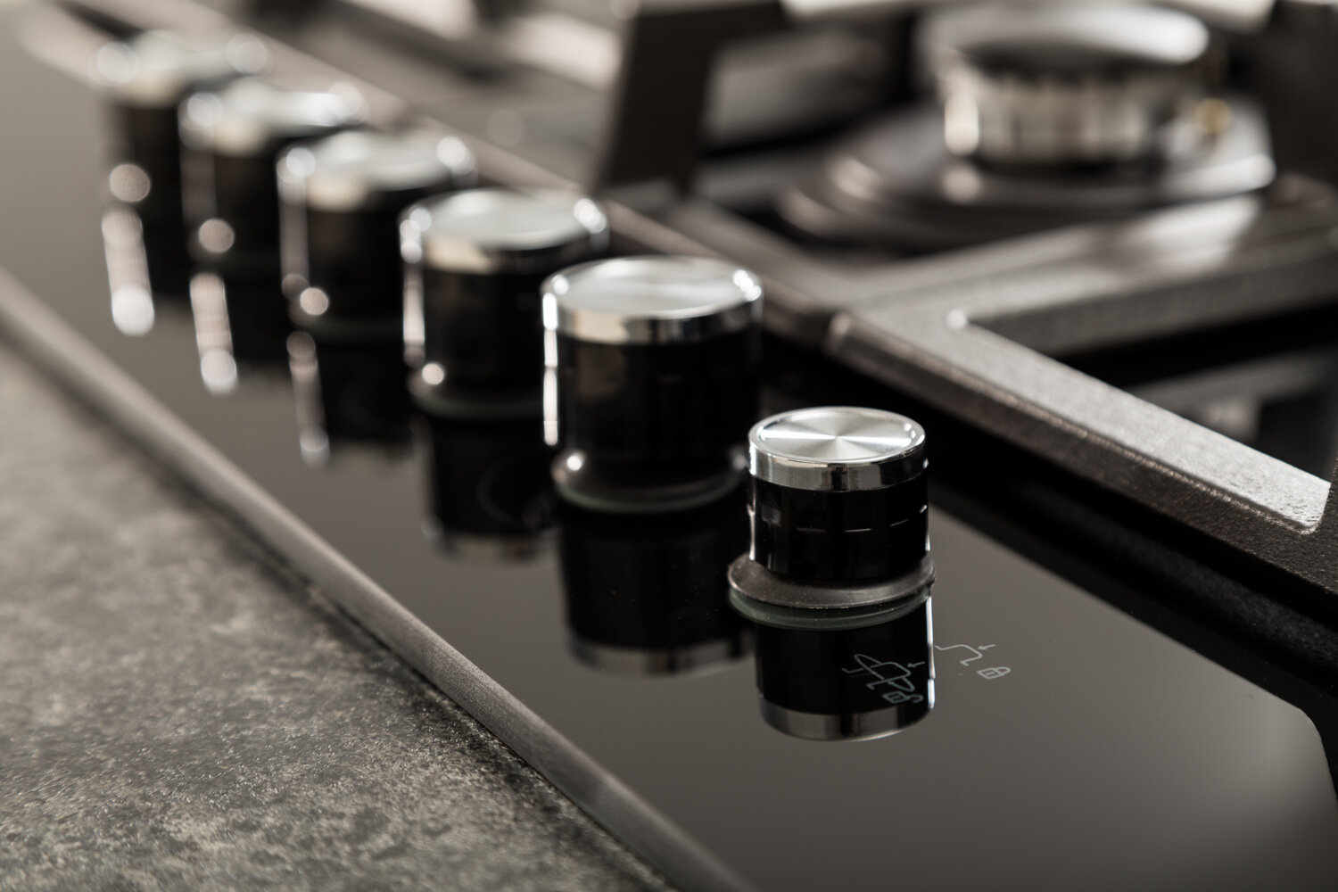 Zbliżenie pokręteł kuchenki gazowej, czarne ze srebrnymi akcentami, na czarnej powierzchni.