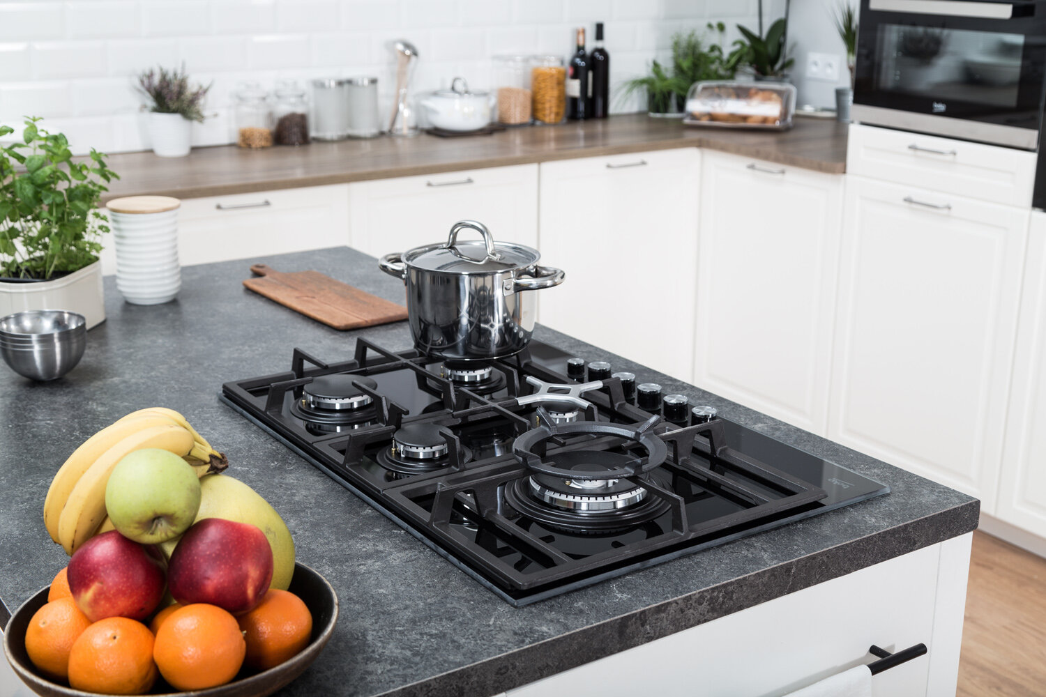 Scena kuchenna z płytą grzejną, miską owoców i innymi akcesoriami kuchennymi.