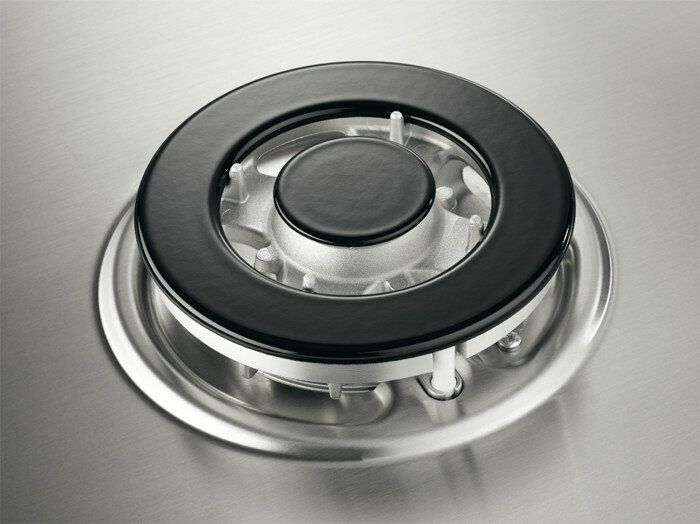 Zbliżenie palnika gazowego na płycie ze stali nierdzewnej, czarna nasadka.