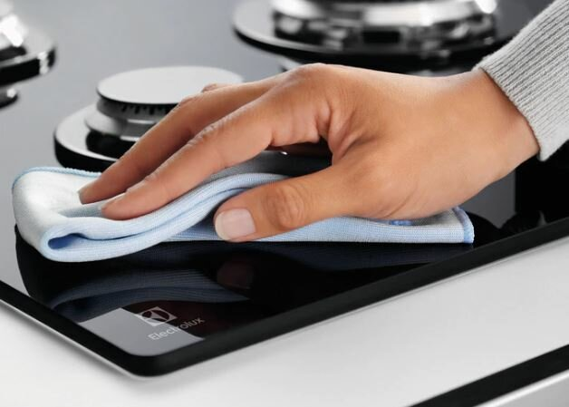 Ręka czyszcząca czarną płytę indukcyjną niebieską szmatką.