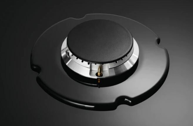 Czarny palnik kuchenki gazowej o okrągłym kształcie. Błyszcząca czarna powierzchnia. Metalowa dysza pośrodku.