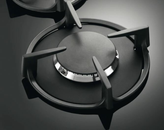 Zbliżenie czarnego palnika kuchenki gazowej z czterema wspornikami i centralnym pierścieniem.