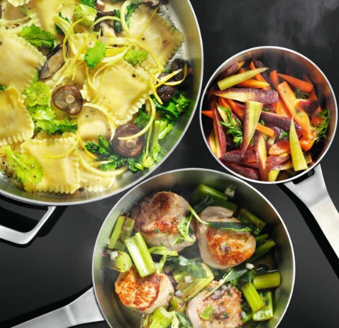 Trzy patelnie z ugotowanym jedzeniem: ravioli, marchew i smażone mięso.